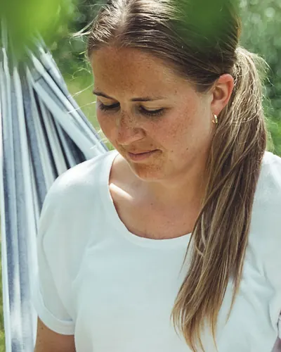 Anette leser i en hengekøye under trærne