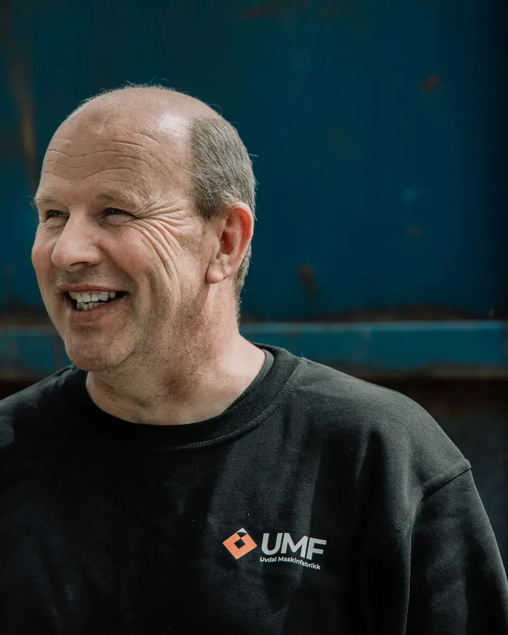 Ole Reidar ler og ser til siden, i svart UMF-genser foran en blå ståldør.